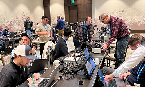 People gather around electronic devices at Plugfest 2026.