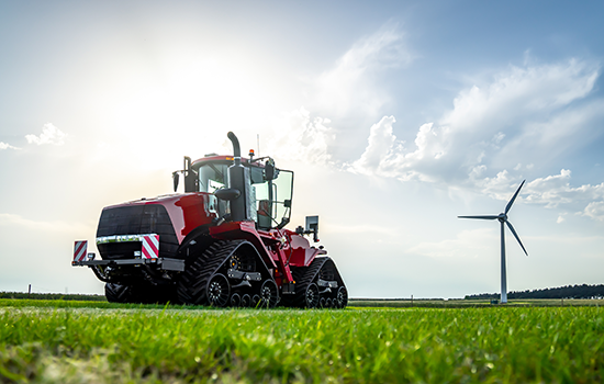 A red agricultural tractor in a green field with a wind turbine in the background