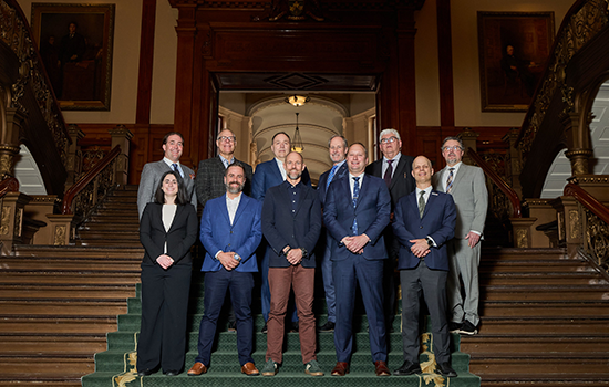 Group of professionally dressed individuals standing on a grand staircase inside a historic government building in Ontario during AEM’s inaugural Queen’s Park Day